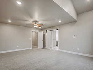 Unfurnished bedroom featuring a barn door, light colored carpet, recessed lighting, ceiling fan, and connected bathroom