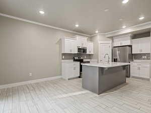 Kitchen featuring a breakfast bar area, appliances with stainless steel finishes, white cabinets, tasteful backsplash, and crown molding