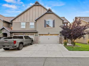 View of front facade featuring a garage, stone siding, driveway, and stucco siding