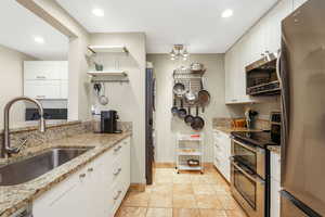 Kitchen with appliances with stainless steel finishes, white cabinetry, open shelves, light stone counters, and recessed lighting