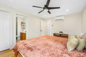 Bedroom featuring light wood-style flooring, recessed lighting, ceiling fan, a wall mounted air conditioner, and connected bathroom