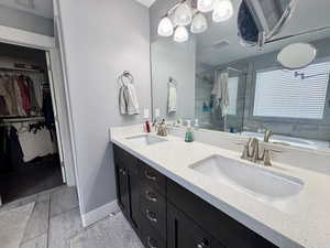 Primary Full bath featuring a walk in closet, a shower stall, double vanity, and a chandelier