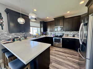 Kitchen with appliances with stainless steel finishes, a peninsula, light stone counters, a breakfast bar, and hanging light fixtures