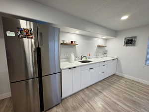 Kitchen with white cabinets, freestanding refrigerator, open shelves, a textured ceiling, and light wood finished floors