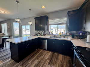 Kitchen with stainless steel appliances, hanging light fixtures, open floor plan, dark wood-style floors, and a peninsula
