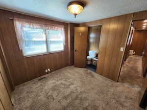 Unfurnished bedroom featuring wood walls, carpet flooring, a textured ceiling, and ensuite bathroom