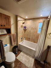 Full bathroom featuring shower / bathtub combination with curtain, a textured ceiling, and dark tile patterned flooring