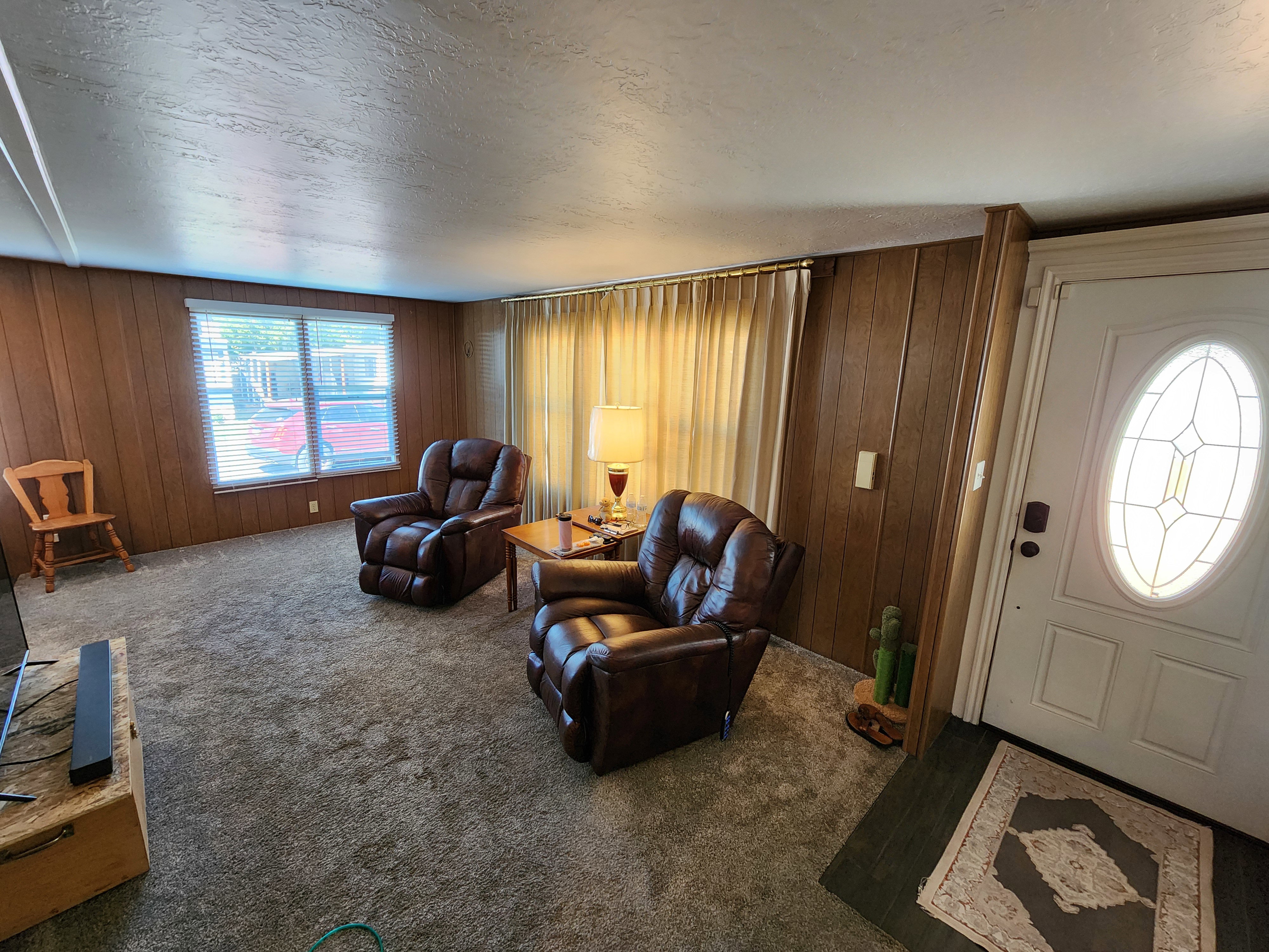 Living area with a textured ceiling, carpet flooring, and wood walls
