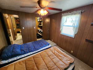 Bedroom featuring carpet floors, wooden walls, a ceiling fan, and a closet