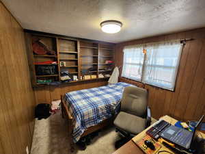Carpeted bedroom with wood walls and a textured ceiling