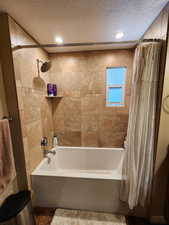 Bathroom with shower / bathtub combination with curtain and a textured ceiling