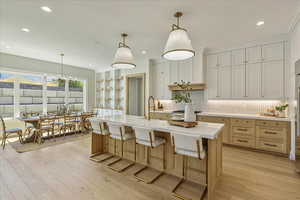 Kitchen with hanging light fixtures, light wood-style floors, a kitchen bar, decorative backsplash, and open shelves