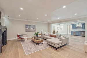Living room with a fireplace, recessed lighting, light wood-style floors, bar with sink, and ornamental molding