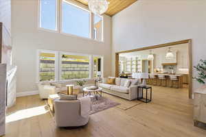 Living room with light wood-style floors, a fireplace, a chandelier, wooden ceiling, and a high ceiling