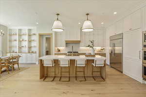 Kitchen with white cabinetry, decorative light fixtures, a center island with sink, a kitchen bar, and recessed lighting