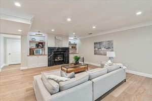 Living room featuring recessed lighting, light wood-type flooring, a large fireplace, ornamental molding, and built in features