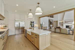 Kitchen with light brown cabinetry, light wood finished floors, open floor plan, decorative light fixtures, and backsplash