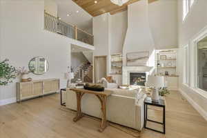 Living room featuring light wood finished floors, a glass covered fireplace, built in features, recessed lighting, and a high ceiling