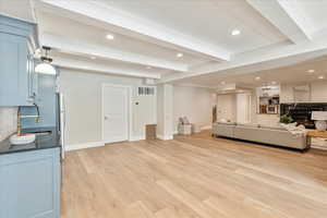 Living area with beamed ceiling, recessed lighting, ornamental molding, light wood-style floors, and a premium fireplace