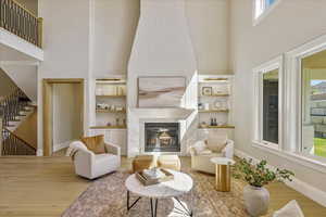 Living room with a towering ceiling, wood finished floors, a glass covered fireplace, stairs, and built in features