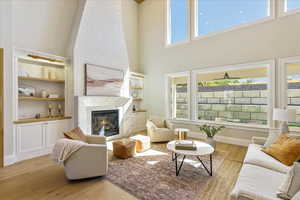 Living area featuring light wood-style flooring, a towering ceiling, a premium fireplace, and built in shelves