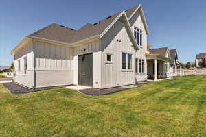 Rear view of house featuring board and batten siding, a lawn, roof with shingles, and a patio area