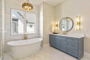 Full bath featuring light marble finish flooring, vanity, a freestanding bath, and tile walls