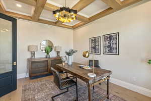 Office featuring light wood-style flooring, a chandelier, beamed ceiling, coffered ceiling, and crown molding