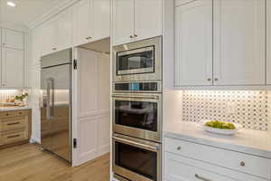 Kitchen with decorative backsplash, built in appliances, white cabinets, light wood-style floors, and light stone counters