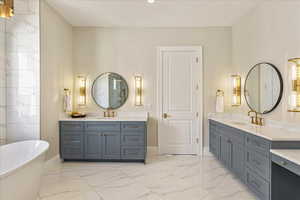 Bathroom featuring light marble finish floors, a freestanding tub, and two vanities