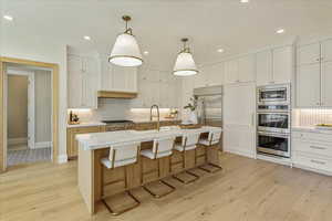 Kitchen with backsplash, a breakfast bar, hanging light fixtures, white cabinets, and recessed lighting