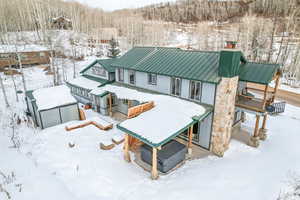 Snow covered house featuring a metal roof, a wooded view, a chimney, and a standing seam roof