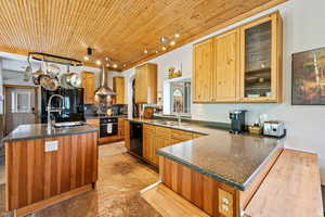 Kitchen featuring backsplash, glass insert cabinets, a peninsula, wall chimney exhaust hood, and black appliances