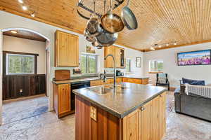 Kitchen featuring track lighting, a center island with sink, wood ceiling, dark countertops, and open floor plan