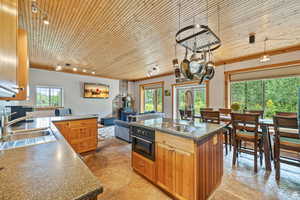 Kitchen featuring wooden ceiling, brown cabinets, oven, a kitchen island with sink, and dark countertops