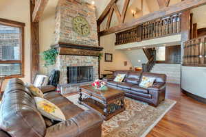 Living area with wood finished floors, high vaulted ceiling, a stone fireplace, stairway, and beam ceiling