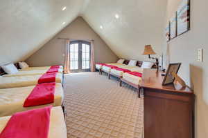 Bedroom featuring a textured ceiling, french doors, light carpet, access to exterior, and vaulted ceiling
