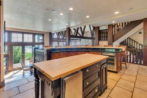 Kitchen with stone tile flooring, a kitchen island, wine cooler, recessed lighting, and butcher block countertops