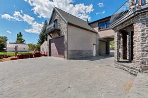 View of side of home featuring stucco siding, stone siding, an attached garage, a balcony, and decorative driveway