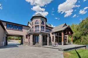 View of front of home featuring stone siding, a patio, stucco siding, and a balcony
