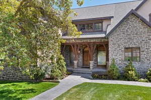 View of front of property with a high end roof, a porch, a front lawn, and stone siding