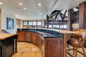 Kitchen with a breakfast bar area, a textured ceiling, open floor plan, stone tile flooring, and brown cabinets