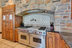 Kitchen featuring range with two ovens, brown cabinets, dark stone counters, and backsplash