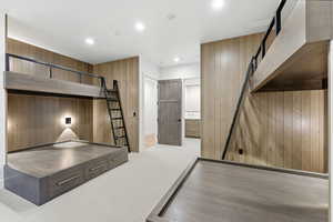 Unfurnished bedroom with wooden walls, a barn door, recessed lighting, ensuite bathroom, and light carpet