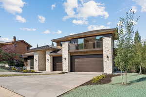 View of front of house featuring concrete driveway, a balcony, stone siding, and a garage