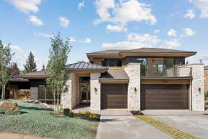 Prairie-style house with stone siding, concrete driveway, a balcony, a garage, and a shingled roof