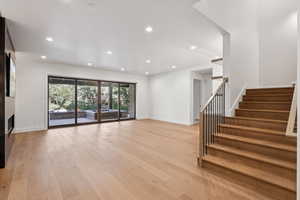 Unfurnished living room with recessed lighting, light wood-style flooring, a glass covered fireplace, and stairs