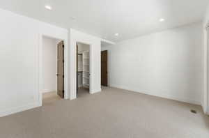 Unfurnished bedroom featuring a walk in closet, light carpet, and recessed lighting