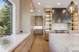 Kitchen featuring light stone countertops, light wood-type flooring, hanging light fixtures, backsplash, and recessed lighting