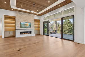 Unfurnished living room with wooden ceiling, built in shelves, light wood-type flooring, a fireplace, and a tray ceiling